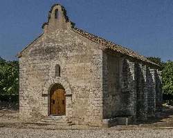 Small stone church with wooden door and bell tower in a rural landscape.