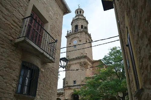 Vista de la torre de la Iglesia de San Cemeterio y San Celedonio, entre dos casas del pueblo con una ventana y balcón