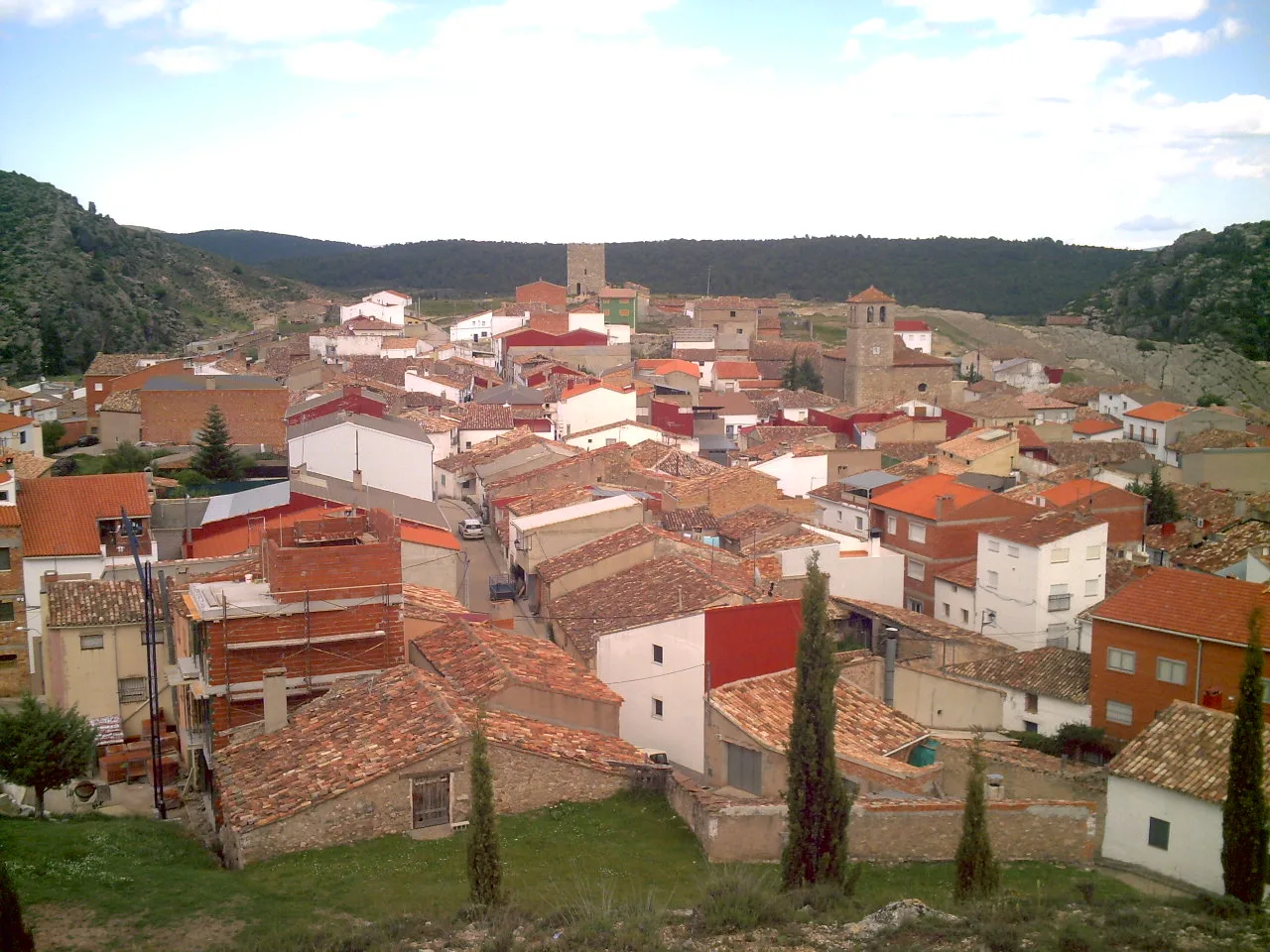 Vista panorámica de Henarejos con tejados de tejas y montañas de fondo.