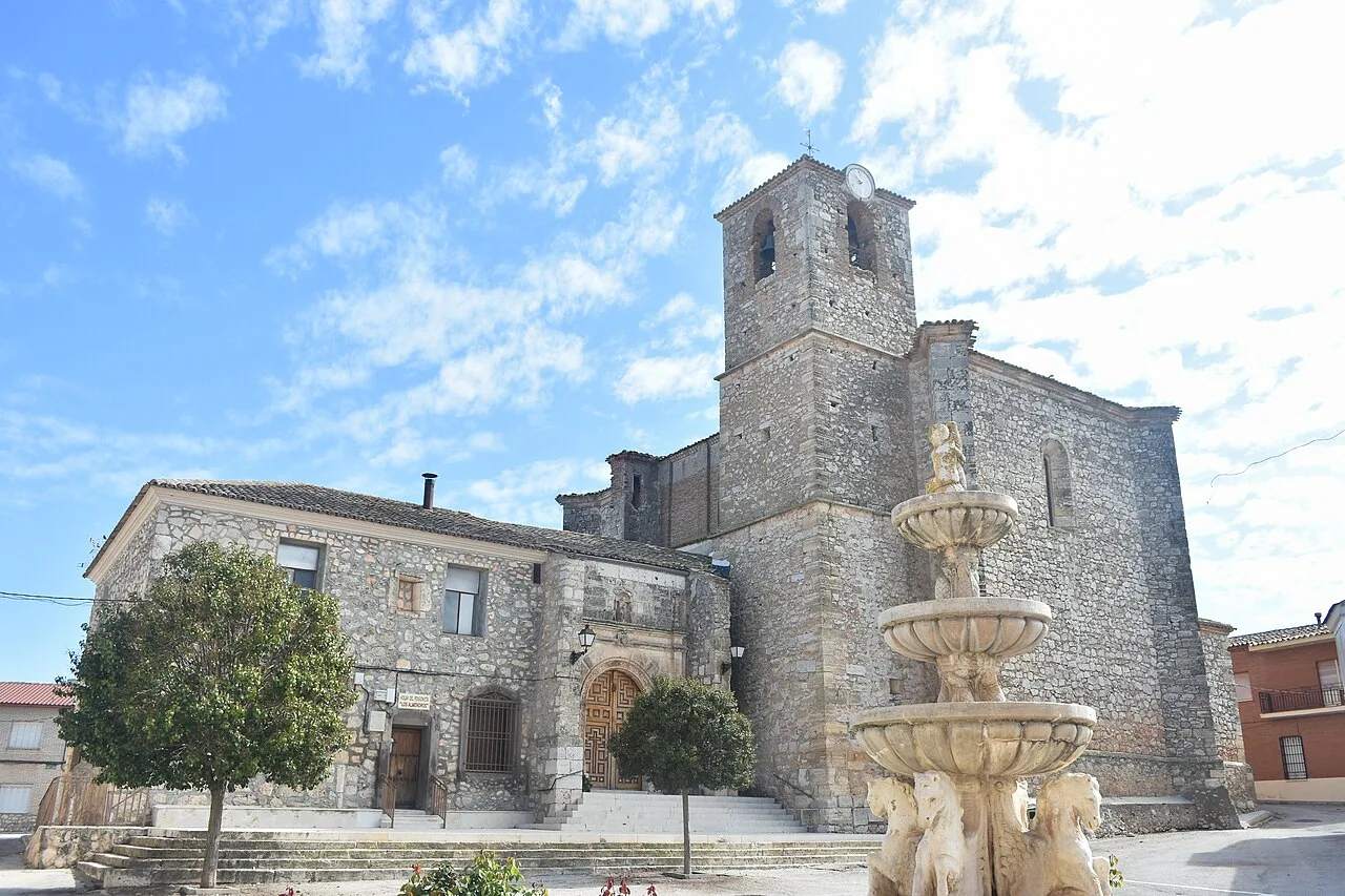 Steinkirche von Almendros mit Brunnen und Bäumen drumherum.