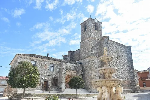 Steinkirche von Almendros mit Brunnen und Bäumen drumherum.