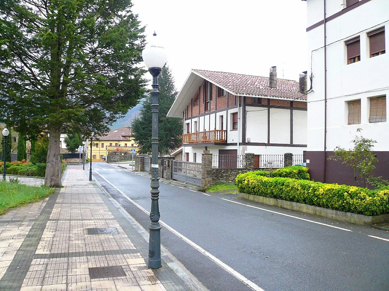 Calle con farolas, árboles y casas en barrio de Zubiaur, Orozko.