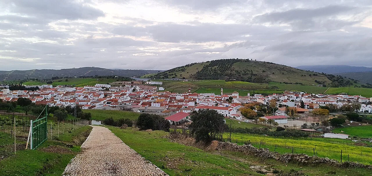 Vista de un pueblo con casas blancas y colinas verdes en el fondo.