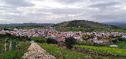 Vista de un pueblo con casas blancas y colinas verdes en el fondo.