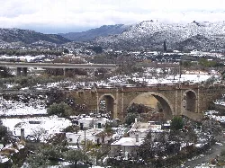 Puente de piedra sobre un río con nieve y montañas nevadas.