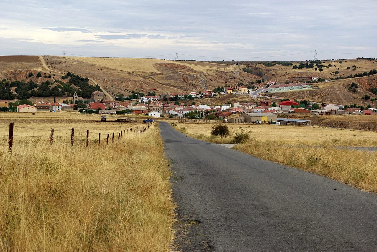 Asphalt road in open countryside with a village in the distance.