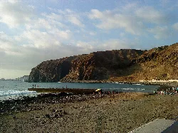 Sandy beach with cliffs and people on the shore in Arona.