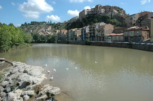 Blick auf den Fluss Cardener in Súria mit Häusern auf dem Hügel und Bäumen am Ufer.