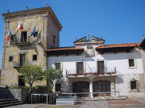 Edificio con torre y fachada blanca, banderas en la torre y balcón con flores.