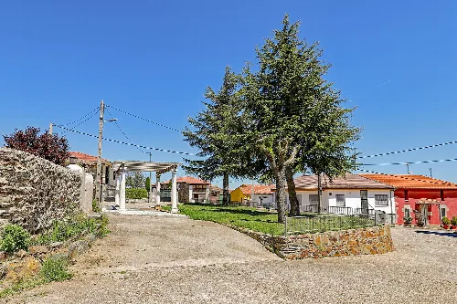 Gepflegter Platz mit Bäumen und Häusern in Herguijuela del Campo.