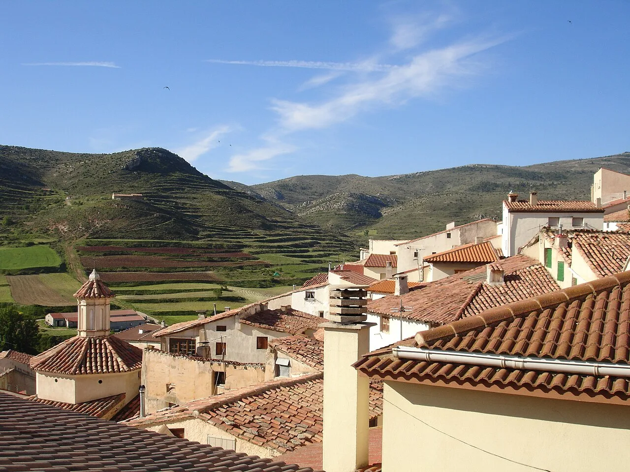 Tejados y casas en Ejulve con terrazas agrícolas en las colinas de fondo.
