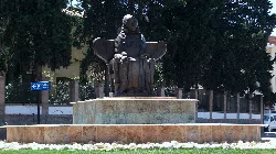 A statue of a seated woman wearing a long dress and cloak, in a roundabout.