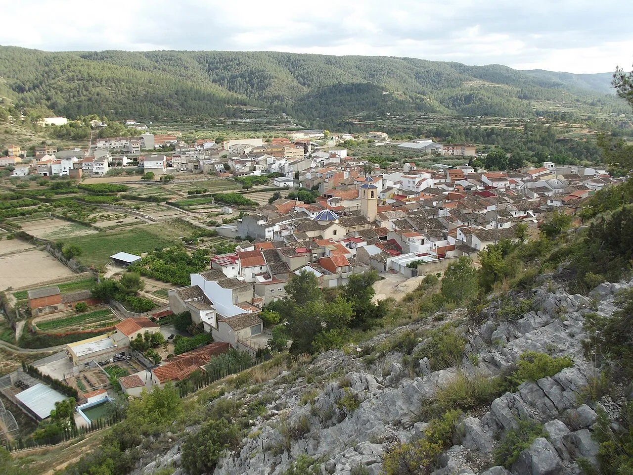 Vista de un pueblo con casas y campos en un valle rodeado de montañas.