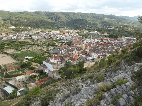 Blick auf eine Stadt mit Häusern und Feldern in einem Tal, umgeben von Bergen.