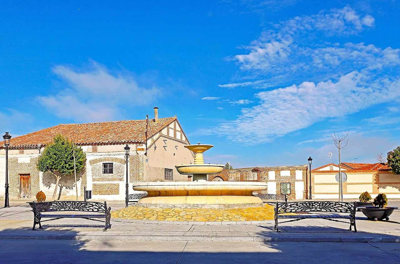 Fuente en la plaza de Rasueros con casas y bancos alrededor.