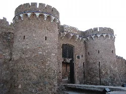 Puerta de castillo con torres redondas de piedra y almenas.