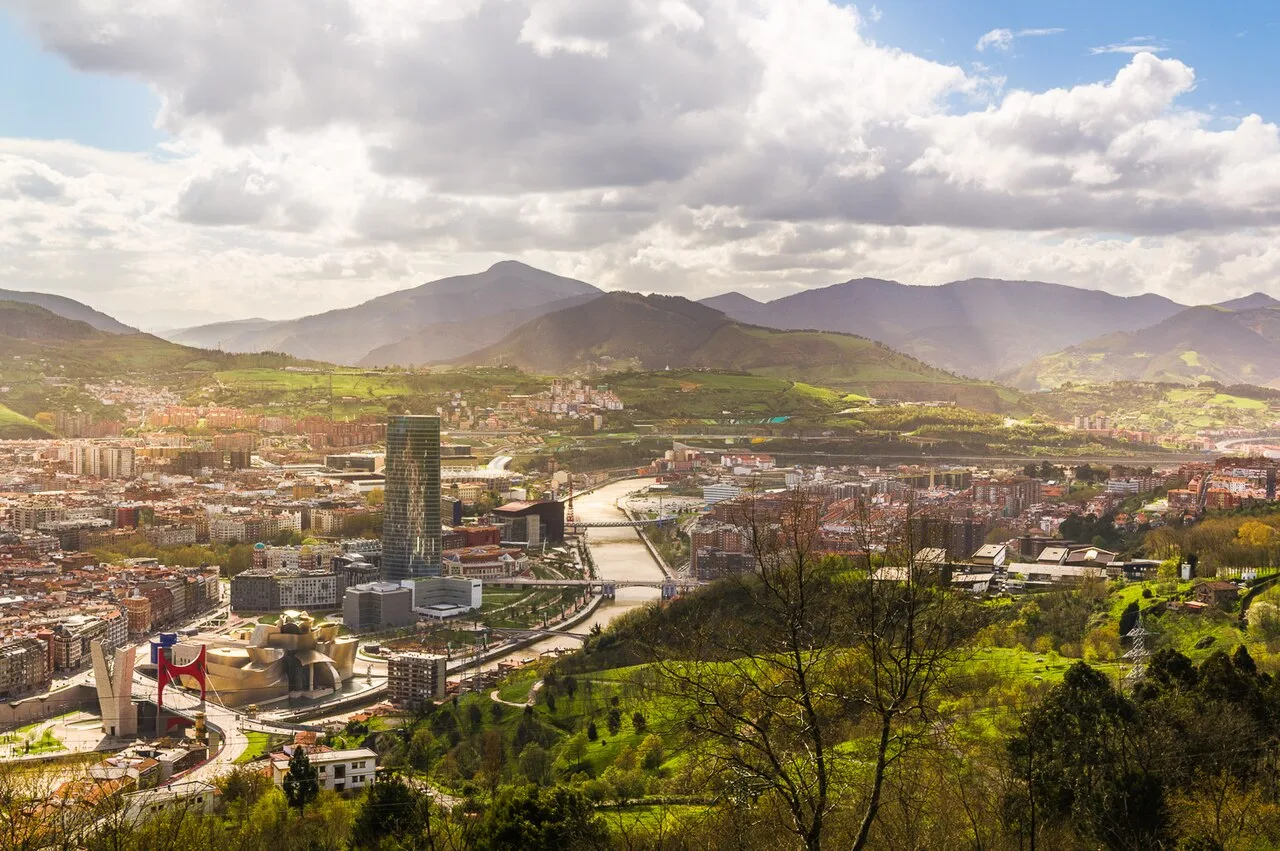 Vista panorámica de Bilbao con río, colinas y montañas.