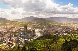 Vista panorámica de Bilbao con río, colinas y montañas.