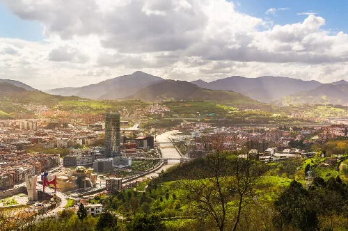 Panoramic view of Bilbao with river, hills, and mountains.
