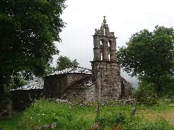 Fachada de una iglesia con campanario en Muras, Lugo, rodeada de árboles y césped.