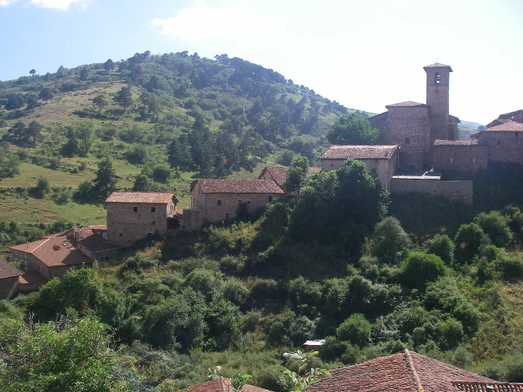 Vista de casas de piedra y una iglesia en una colina rodeada de vegetación y montañas.