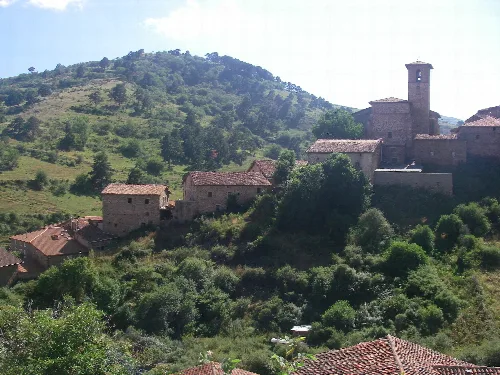 Aussicht auf Steinhäuser und eine Kirche auf einem Hügel, umgeben von Vegetation und Bergen.