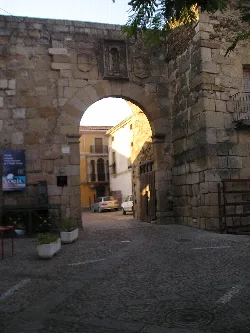 Steinernes Tor in der Stadtmauer von Coria mit Gebäuden und Autos im Hintergrund.