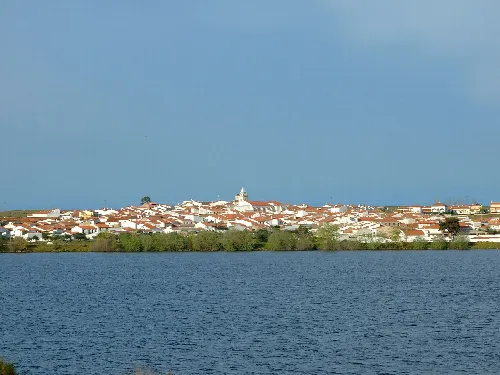 Blick auf Membrío vom Stausee, mit Häusern und einer Kirche im Hintergrund.