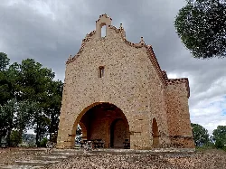 Pequeña ermita de piedra con arcos y un cielo nublado en Aguaviva.