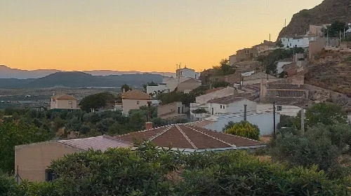 Paisaje con casas en la ladera y montañas en la distancia.