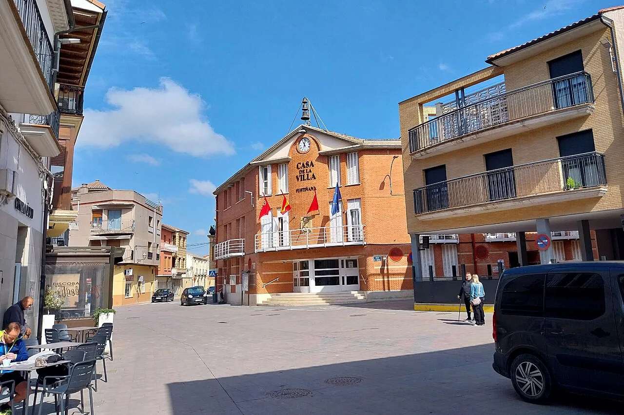 Plaza con edificios y personas en Fustiñana, Navarra, en un día soleado.