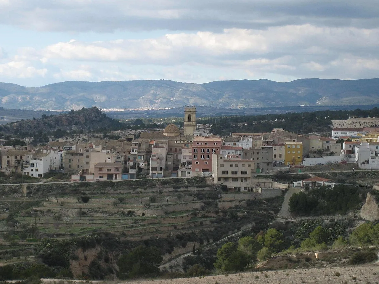 Landschaft von Tibi mit Häusern, Schloss und Bergen im Hintergrund.