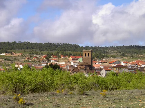 Blick auf eine Stadt mit Kirche und Häusern, umgeben von Vegetation und Hügeln.