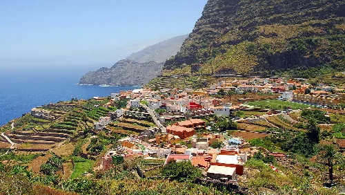 Colorful houses on a hillside with mountains and sea in the background.