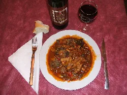 Plato de chanfaina con vino y pan en una mesa.