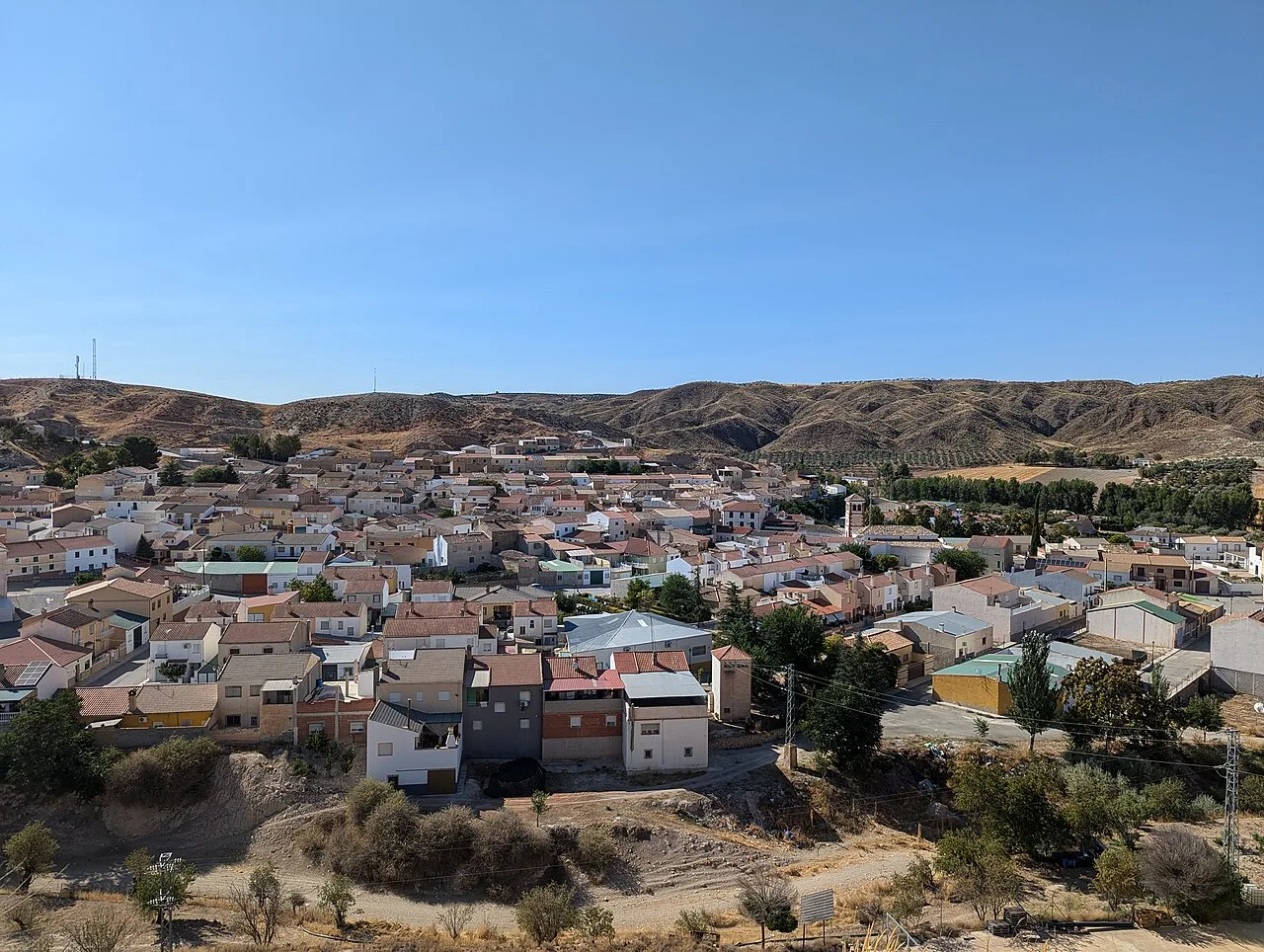 Panoramablick auf Alamedilla von einem Aussichtspunkt, mit Häusern und Hügeln im Hintergrund.