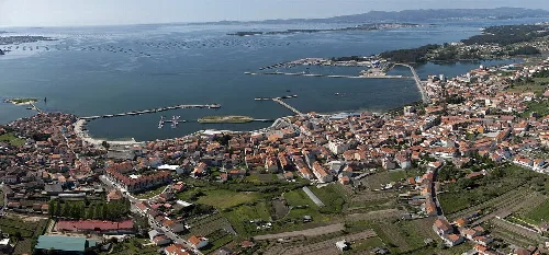 Vista aérea de un pueblo costero con puerto, edificios y campos verdes.