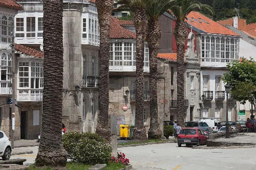 Edificios en Corcubión con palmeras y coches en la calle.