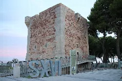 Steinerne Turm mit dicken Wänden und einem kleinen Turm, umgeben von Geländern und Bäumen.