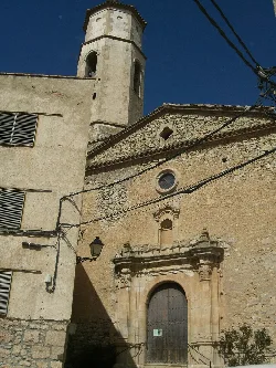 Fachada de piedra de la iglesia Sant Andreu con torre en Arbolí.