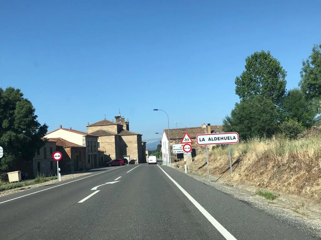 Carretera en La Aldehuela con señal de entrada y edificios antiguos.