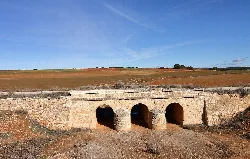 Stone bridge with three arches in a landscape of fields and blue sky.