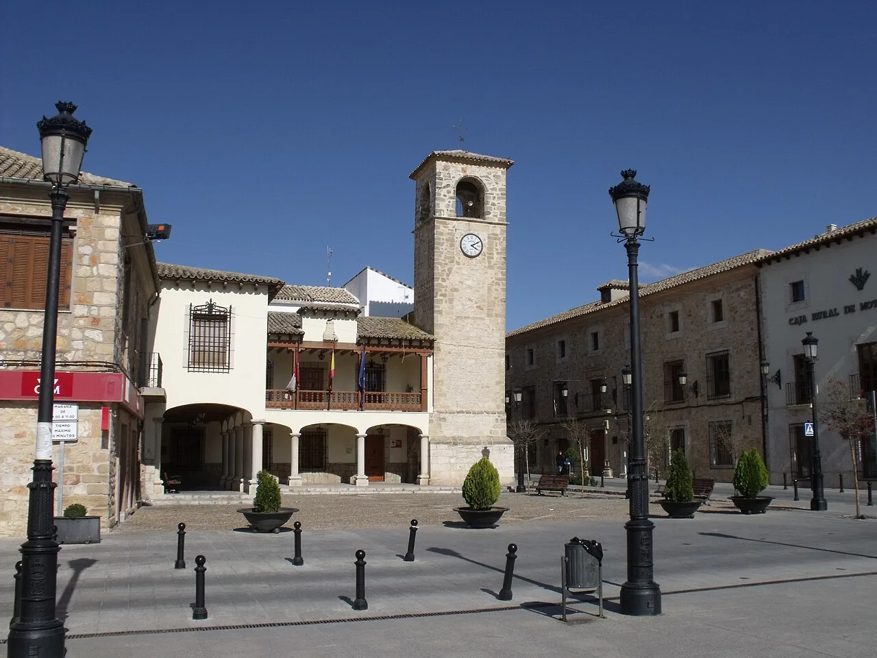 Main square with clock, lampposts, and stone buildings in Mota del Cuervo.