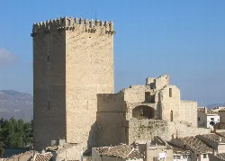 Medieval castle tower in Moratalla, Murcia, with surrounding walls and rooftops.