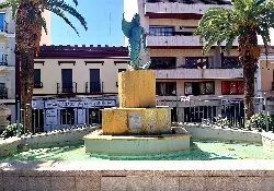 Fountain with the Sirena sculpture in a park with palm trees and buildings in the background.