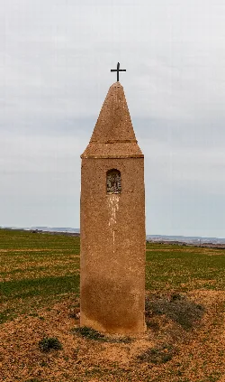 Brown peirón with a cross at the top and a niche with a religious image.