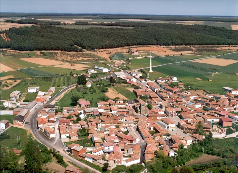 Vista aérea de un pueblo con casas de tejados rojos, campos y bosques en Palencia.