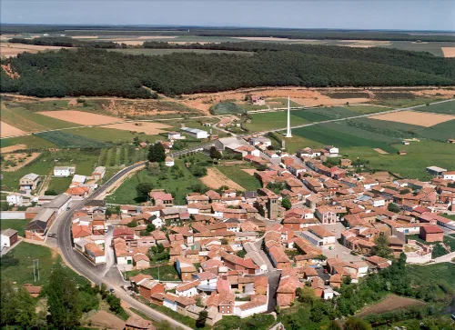 Aerial view of a village with red roofs, fields, and forests in Palencia.