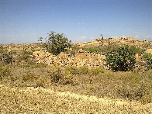 Reste eines mittelalterlichen Bauwerks mit Steinmauern und Vegetation in einer trockenen Landschaft.