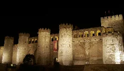 Castle facade with towers and walls lit up at night.